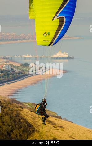 Beachy Head, Eastbourne, East Sussex, Regno Unito. 22nd Mar 2022. Un'altra gloriosa giornata di primavera sulla costa meridionale con vento dal Sud Est porta i piloti del parapendio al sito che si affaccia sulla città di Eastbourne e la spiaggia. Vista del molo attraverso le linee di rigging. Credit: David Burr/Alamy Live News Foto Stock