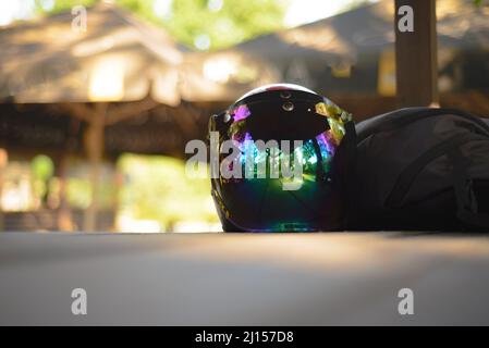 Un casco per motociclette con visiera a specchio si trova sul tavolo con uno zaino da viaggio. Foto Stock
