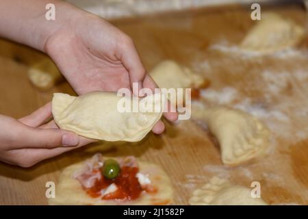 Le mani femminili tengono una torta pugliese chiamata panzerotti, fatta con salsa di pomodoro, mozzarella e prosciutto. Facendo una tradizionale frittura di torte pugliesi, i Foto Stock