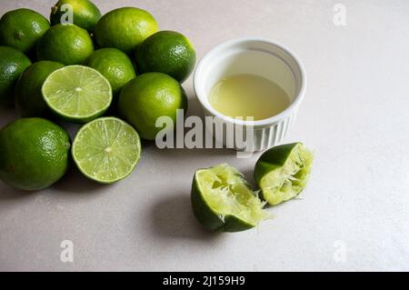 Diversi limoni su sfondo bianco e una frutta spaccata che mostra la polpa e un'altra spaccata già schiacciata con il succo all'interno di un contenitore bianco Foto Stock