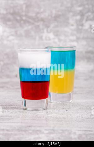 Due cocktail nei colori delle bandiere russe e ucraine su sfondo grigio Foto Stock