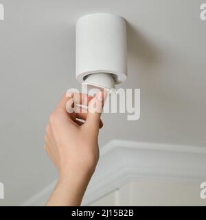 Una donna cambia una lampadina a risparmio energetico a soffitto con lampada a LED in un salotto di casa. Lavori in altezza, fai da te Foto Stock