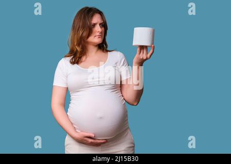 Carta igienica nelle mani di una donna incinta, studio girato su uno sfondo blu Foto Stock