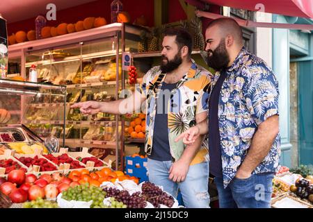 Giovane coppia gay che acquista frutta al mercato all'aperto. Concetto di stile di vita sano. Foto Stock