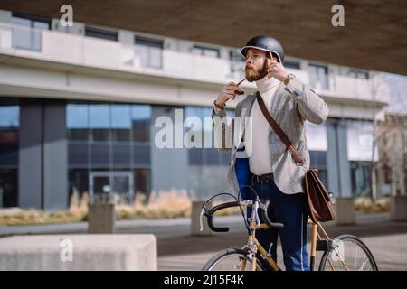 Il giovane uomo d'affari sta mettendo sul casco prima della bicicletta ride.Travel al lavoro. Sicurezza e trasporto ecologico Foto Stock