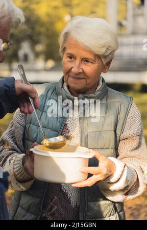 Donna caucasica anziana in abbigliamento casual riceve cibo da un uomo, guarda l'uomo sfondo parco persone anziane benessere sostegno concetto medio shot fuoco selettivo . Foto di alta qualità Foto Stock