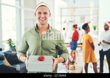 Santa segreta è la mia tradizione di ufficio preferita. Ritratto di un bel giovane uomo d'affari che tiene una confezione regalo in un ufficio festa di Natale con i colleghi Foto Stock