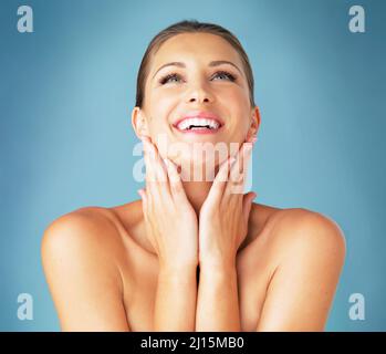 Questa crema al collo sta lavorando meraviglie. Studio girato di una bella giovane donna sentendo la sua pelle su uno sfondo blu. Foto Stock