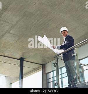 Passando attraverso i piani come il capo che è. Ritratto di un allegro architetto maschile professionista che guarda la fotocamera mentre tiene i progetti all'interno Foto Stock