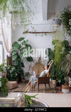 Donna felice e rilassata che si diverta a lavorare in remoto su un laptop mentre si siede in uno spazio di lavoro ispirato alla natura Foto Stock