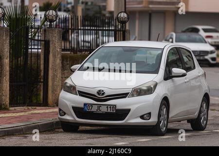 Side; Turchia – Marzo 03 2022: Toyota Yaris bianco è parcheggiato sulla strada in una giornata calda sullo sfondo di un edificio, recinzione Foto Stock