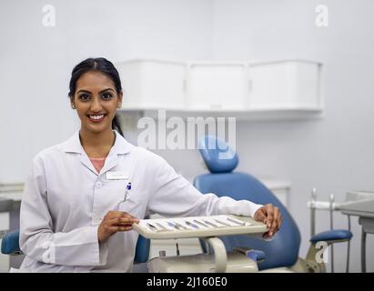 La salute orale è una parte essenziale di una vita sana. Ritratto di una giovane dentista femminile seduto accanto ad un vassoio di strumenti chirurgici nel suo ufficio. Foto Stock