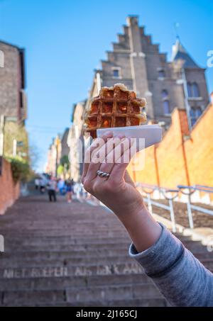 Deliziosi waffle belgi tenuti di fronte allo sfondo sfocato della scalinata Montagne de Bueren a Liege, che è una delle principali attrazioni turistiche della città Foto Stock