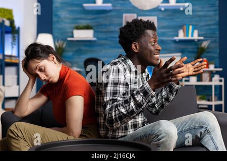 Sconvolto donna caucasica e afroamericana arrabbiato che parla di difficili problemi di relazione. Giovane coppia interrazziale incontrando difficoltà di matrimonio mentre a casa sul divano. Foto Stock
