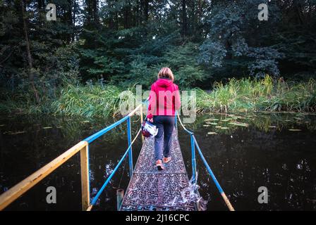 La ragazza con un casco attraversa un ponte sul fiume. La ragazza attraversa il fiume sul ponte Foto Stock