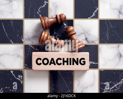Pedine da scacchi che giacciono sulla scacchiera con la parola coaching su un blocco di legno. Foto Stock