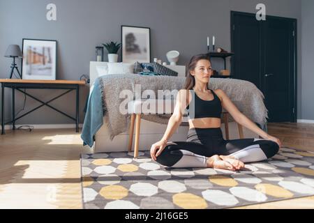 La giovane donna si siede sul pavimento e preme sulle ginocchia allungando i muscoli. Foto Stock