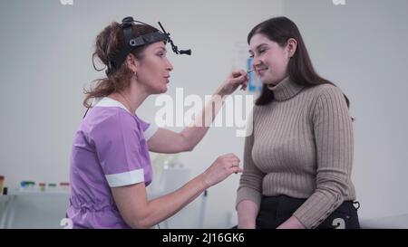 Concetto di otolaringologia. Otorhinolaringologist donna positiva che controlla il naso con otoscopio del suo paziente in ospedale. Congestione nasale, sinusite Foto Stock