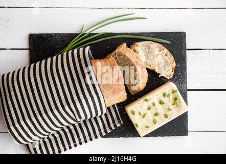 Flat Lay vista appena sfornato farina di grano fatto in casa pane di pane con burro e blocco di burro accanto ad esso su tavola di servizio in pietra nera in cucina casa Foto Stock