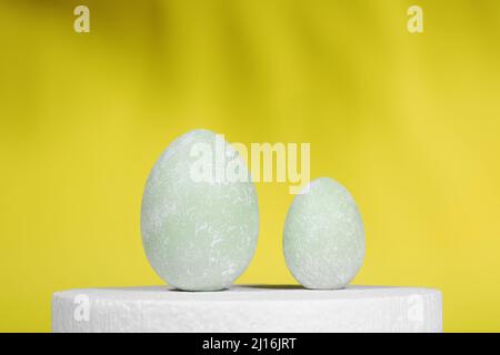 Uova di Pasqua su un supporto bianco, su sfondo giallo con ombre. Sfondo di Pasqua creativo. Minimalismo. Spazio di copia Foto Stock