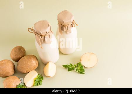 due bottiglie di latte di patata ecologico di tutti i tipi di latte vegetale su sfondo beige con tuberi di patata Foto Stock