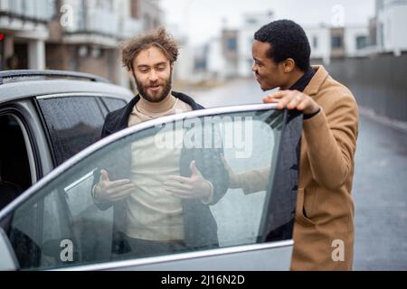 Due uomini flirtare mentre si sta in piedi vicino auto sulla strada Foto Stock
