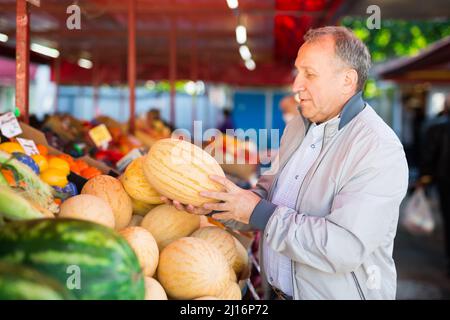 Uomo che sceglie i meloni nel negozio di frutta Foto Stock