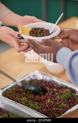 Primo piano verticale medio di volontari irriconoscibili che danno cibo ai poveri in mensa di beneficenza Foto Stock