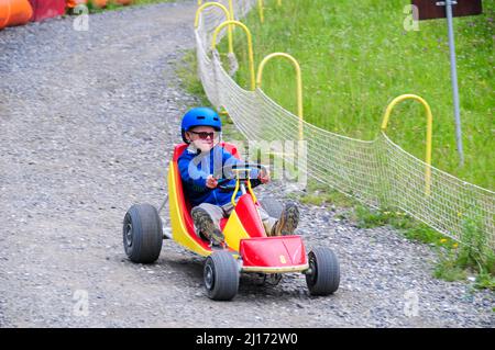 ragazzo giovane che scivola giù collina in un go kart nelle alpi francesi a super devoluy, attività di vacanza, stazione sciistica in estate. Foto Stock