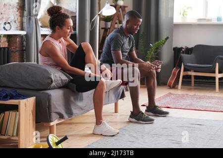 Uomo e donna etnicamente diversi seduti sul divano in soggiorno mettendo su allenatori per uscire per fare jogging al mattino Foto Stock