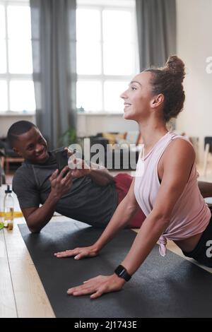 Giovane uomo fotografando la sua fidanzata sportiva praticando esercizi di yoga stretching a casa al mattino Foto Stock