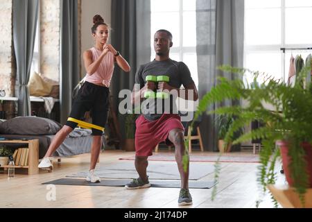 L'uomo e la donna sportivi che fanno esercizi di rinforzo in salotto loft utilizzando la banda di resistenza e manubri Foto Stock