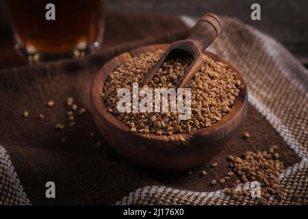 Ciotola di semi secchi di fieno su sfondo di legno scuro. Cibo sano, Ayurveda e concetto di medicina alternativa Foto Stock