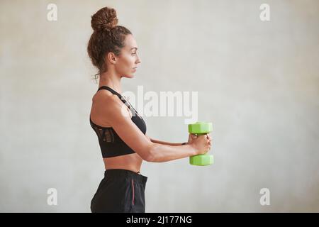 Vista laterale di bella giovane donna caucasica adulto con corpo sottile facendo esercizio con dumbbell in camera mansarda Foto Stock