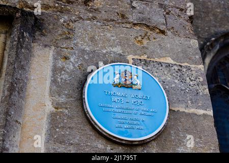 Targa blu sul muro della chiesa di San Pietro del 15th secolo che commemora l'ordinazione di Thomas Wolsey nel 1498, High Street, Marlborough, Wiltshire Foto Stock