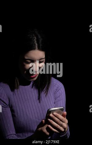donna che guarda il mobile con un'espressione di disgusto su sfondo nero Foto Stock