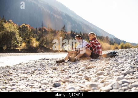 Austria, Alpi, giovane su un viaggio escursionistico avente una interruzione in corrispondenza di un ruscello mappa di lettura Foto Stock