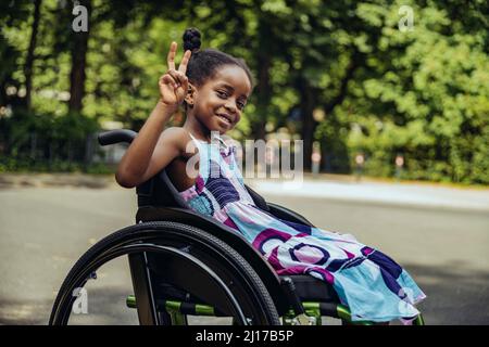 Ragazza disabili in sedia a rotelle che fa segno di pace Foto Stock