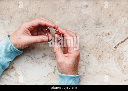 Donna anziana che tiene il cuore a forma di biscotto taglierina Foto Stock