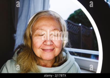 Donna anziana con occhi chiusi, vista attraverso la luce ad anello illuminata Foto Stock