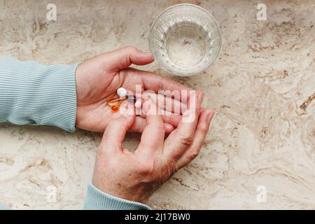 Donna anziana che assume pillole medicinali con un bicchiere d'acqua Foto Stock
