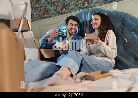 Una coppia felice che ha il sushi seduto sul letto in una nuova casa Foto Stock