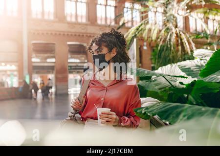 Giovane donna con maschera protettiva alla stazione ferroviaria Foto Stock