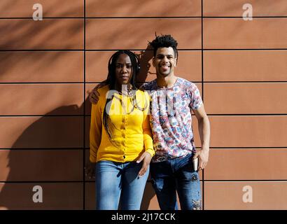 Giovane donna che indossa le cuffie in piedi con il ragazzo di fronte alla parete Foto Stock