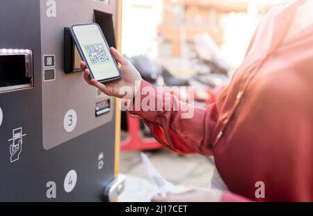 Donna che esegue la scansione del codice QR sulla macchina per biglietti alla stazione Foto Stock