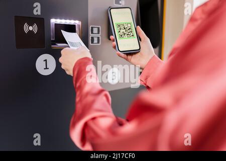 Donna che esegue la scansione del codice QR sulla macchina per biglietti tramite smartphone alla stazione Foto Stock