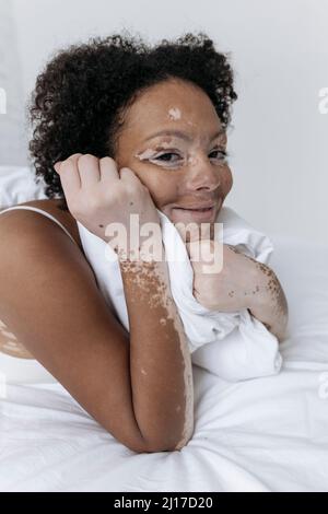 Donna sorridente sdraiata con mano sul mento in camera da letto a casa Foto Stock