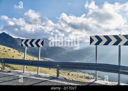 Strada di montagna con il cartello con la freccia del traffico il giorno di sole Foto Stock