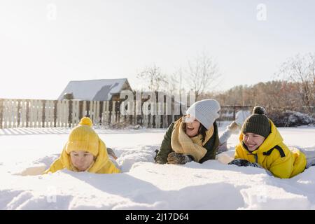 Ragazzi giocosi con la madre sdraiata sulla neve in inverno Foto Stock