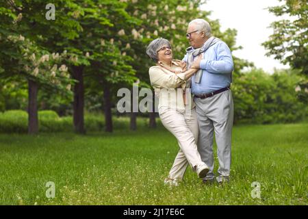 L'uomo anziano e la donna ballano sull'erba verde del parco tra gli alberi. Foto Stock